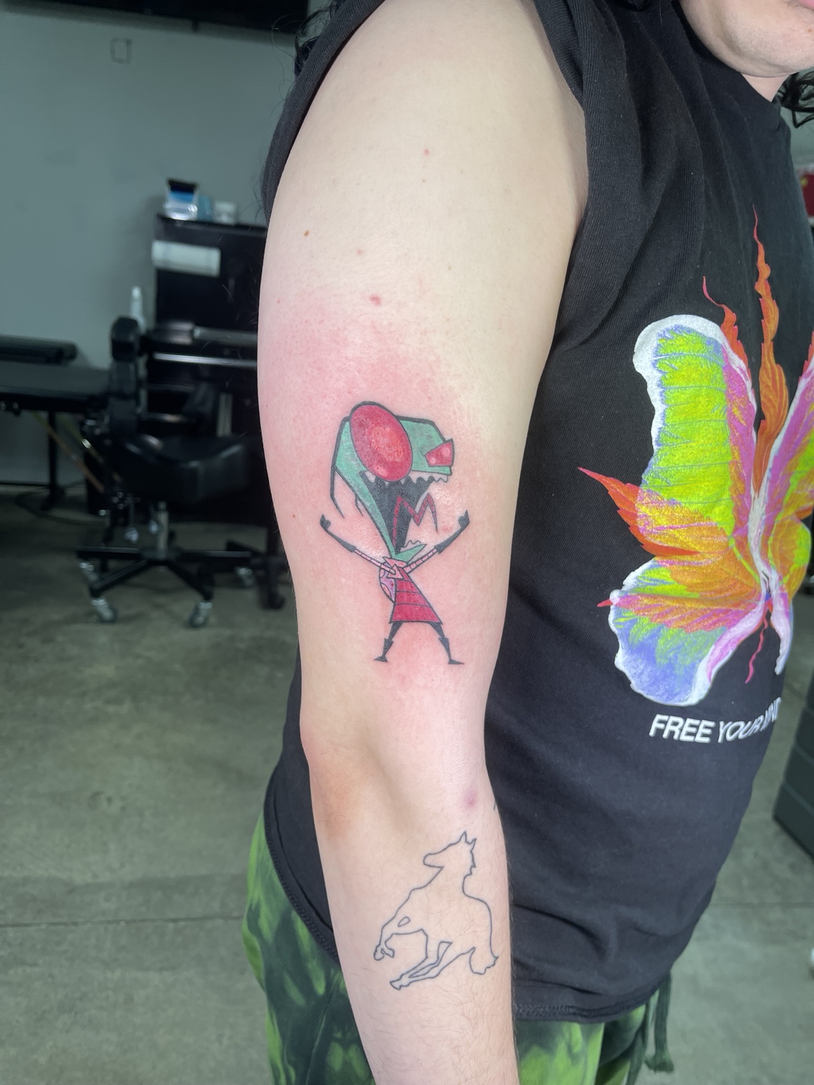 Small colorful character and outline tattoo on upper arm