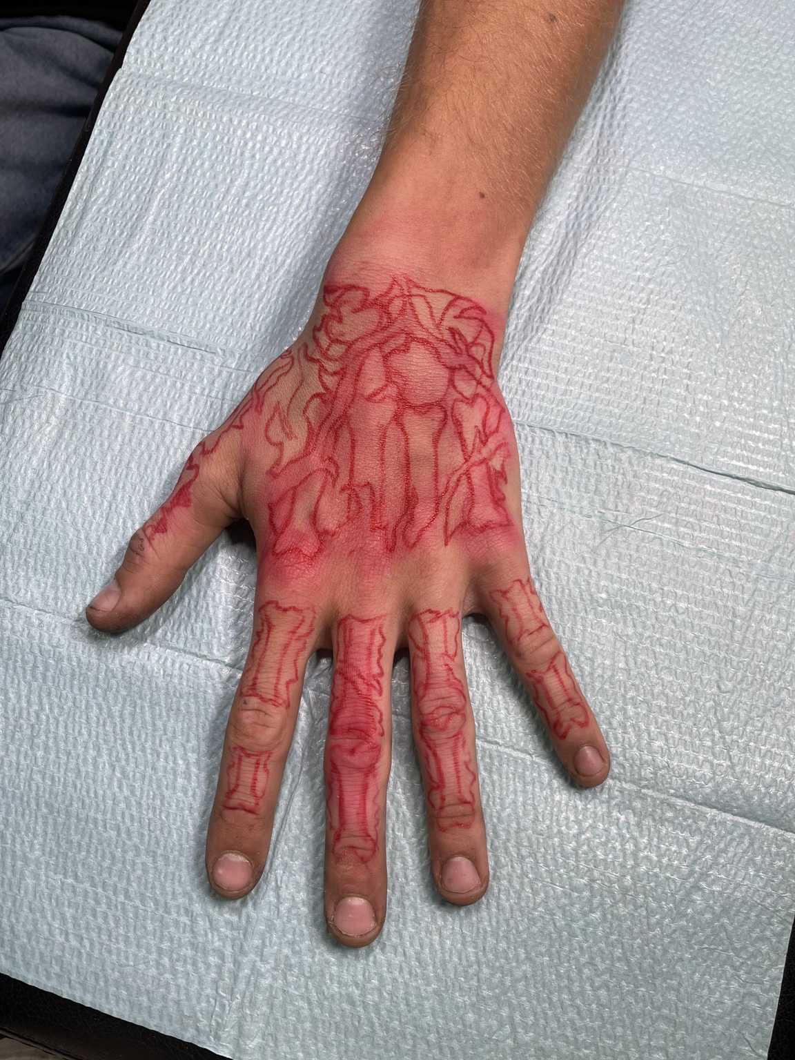 Red layout or transfer drawing on skin before the skeleton hand tattoo was completed
